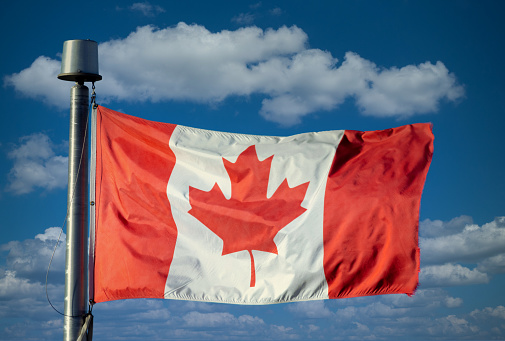 A Waving Canadian flag with a blue sky with clouds