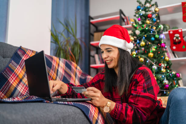 portrait d’une belle jeune femme heureuse avec une chemise rouge assise à la maison, tenant une carte de crédit, faisant des achats en ligne sur un ordinateur portable - christmas office gift people photos et images de collection