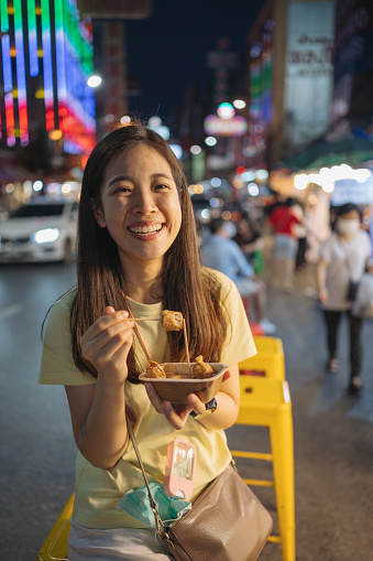 Portrait of a young asian woman, walking on the streets of Bangkok Chinatown district. She is wearing casual street style clothing and enjoy seafood around yaowarat