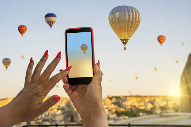 Smartphone in the hands of a woman  taking pictures of a beautiful landscape and balloons in Cappadocia. Sunrise time, dreamy travel concept Smartphone in the hands of a woman  taking pictures of a beautiful landscape and balloons in Cappadocia. Sunrise time, dreamy travel concept ballooning festival stock pictures, royalty-free photos & images