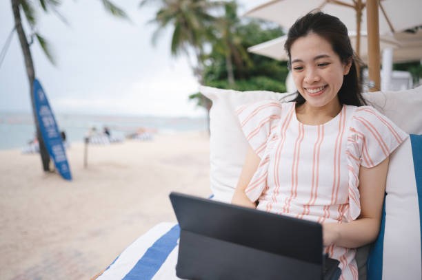 Staycation 5G internet Millennial asian women dress  thai asian enjoy working outdoor with laptop at beach stock photo
