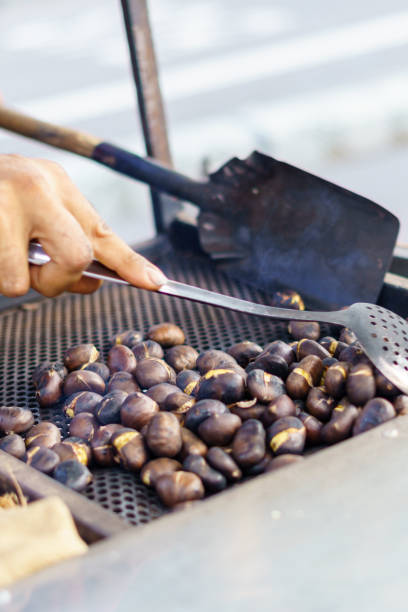 istock Man roasting chestnuts at street stall using metal utensils 1347017928
