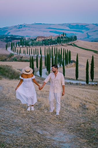 Tuscany, Crete Senesi rural sunset landscape. Countryside farm, cypresses trees, greenfield, sunlight and cloud. Italy, Europe, couple man and woman mid age on vacation in Toscane