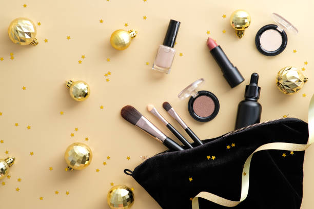 パステルベージュの背景にメイクアップツールと美容製品と化粧品バッグは、ゴールドクリスマスボールと紙吹雪を飾りました。フラットレイ、トップビュー。
