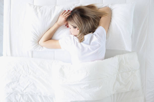 Young woman sleeping on her stomach in white bed top view stock photo