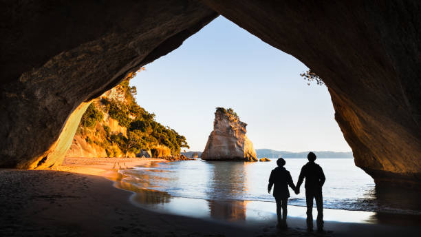 Two people enjoying the view of the Cathedral Cove at sunrise, Coromandel Peninsula, North Island, New Zealand Two people enjoying the view of the Cathedral Cove at sunrise, Coromandel Peninsula, North Island, New Zealand coromandel peninsula stock pictures, royalty-free photos & images