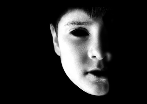 Horizontal portrait of a serious 8 year with white make up. The face looks like spot lit over black background, with copy space for text. Apt for use as posters, backdrops, banners, greeting cards for Halloween Day. There is no text but ample copy space for text. His eyes are like that of a scary ghost.