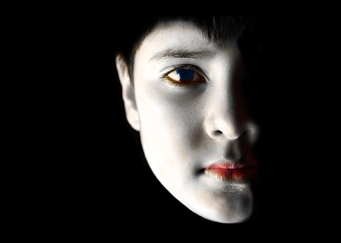 Horizontal portrait of a serious 8 year with white make up. The face looks like spot lit over black background, with copy space for text. Apt for use as posters, backdrops, banners, greeting cards for Halloween Day There is no text but ample copy space for text.