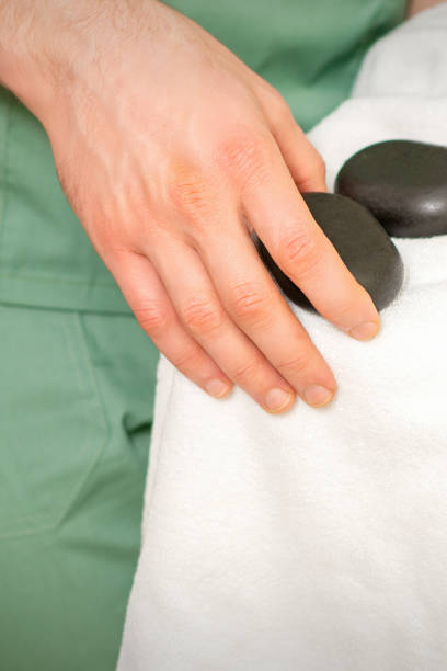 крупным планом руки массажиста протирает черными массажными камнями белое полотенце. - bamboo zen like buddhism spa treatment стоковые фото и изображения