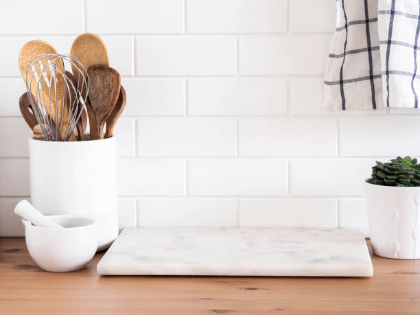 istock Stylish white kitchen background with kitchen utensils standing on wood countertop near white wall tiles 1347032577