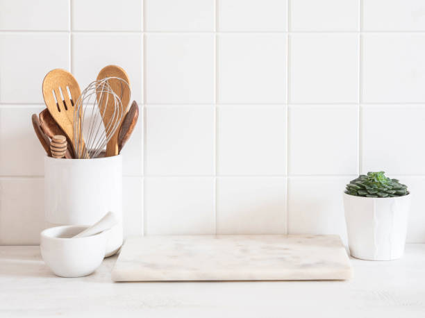 Stylish white kitchen background with kitchen utensils standing on wood countertop near white wall tiles stock photo