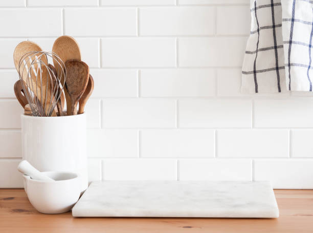 istock Stylish white kitchen background with kitchen utensils standing on wood countertop near white wall tiles 1347032648