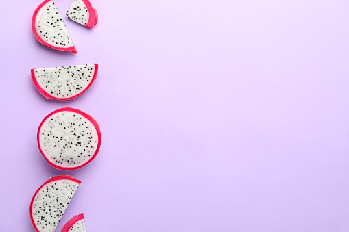 Slices of delicious dragon fruit (pitahaya) on violet background, flat lay. Space for text