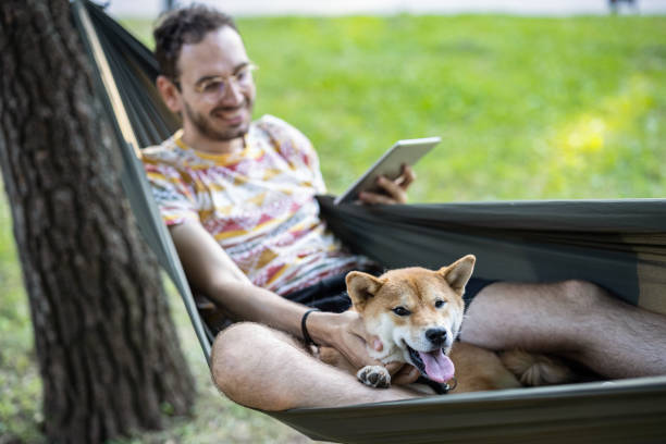 istock Man relaxing with his dog in the park and reading e-book 1347036029