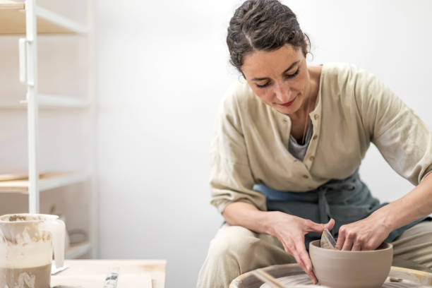 istock Lady siting on bench with pottery wheel and making clay pot 1347038173