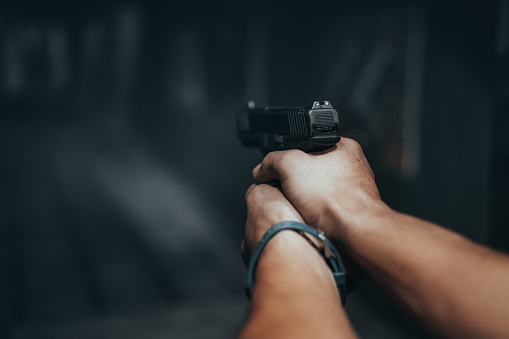 Woman aiming a gun at abandoned house background. With focus on the gun