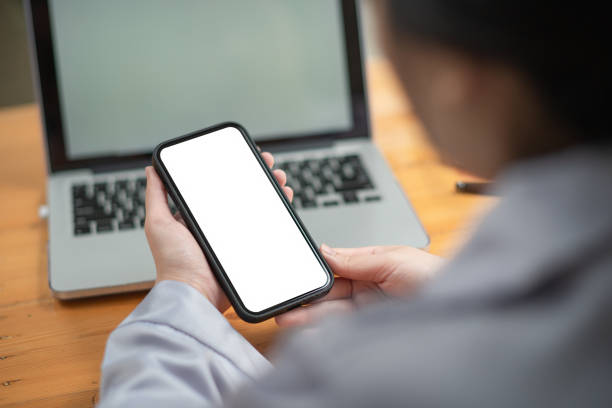 istock Woman holding mobile phone with white screen while sitting at her office desk. 1347043763