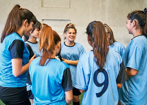 Group of female soccer players standing in a huddle and discussing game plan in soccer court. Girls soccer team playing game strategy at indoor sports court.