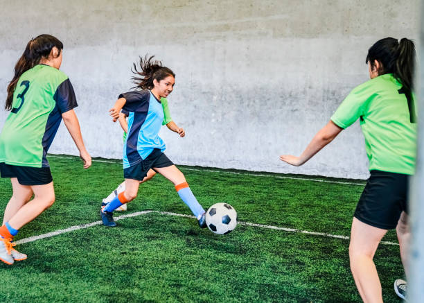 Girls soccer match on sports court Girl soccer player in blue jersey kicking ball towards the goal post. Girls running towards soccer ball during match on sports court. teen goalie stock pictures, royalty-free photos & images