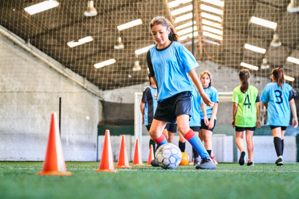 Confident female soccer player practicing skills at court Young girl leading ball between cones on sports court. Female player in blue jersey practicing dribbling skill at court. cone shape photos stock pictures, royalty-free photos & images