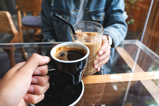 Closeup of a woman and a man clinking coffee cups together in cafe