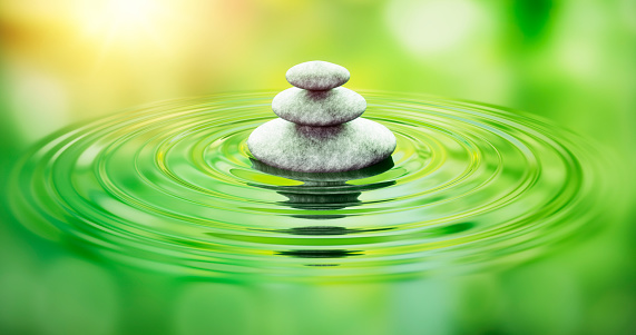 Stack of light gray pebble stones in water ripples with green reflection - zen and nature concept