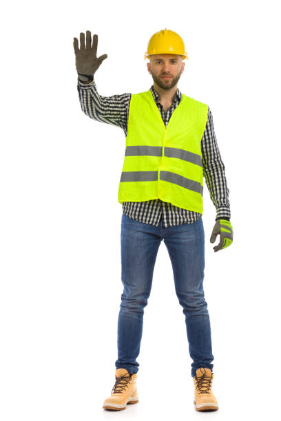 istock Serious construction worker in reflective clothes is standing with hand raised and showing stop gesture. Full length on white background. 1347048651