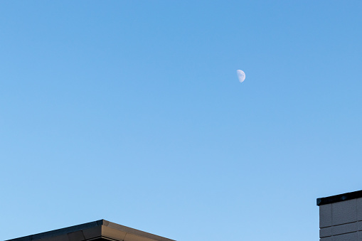 Half moon floating in the blue sky above the building