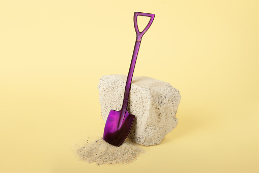 Decorative shovel staying near stone.Quartz sand on the yellow background. Construction and transportation concept.