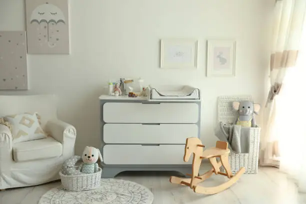 Beautiful baby room interior with toys, armchair and modern changing table