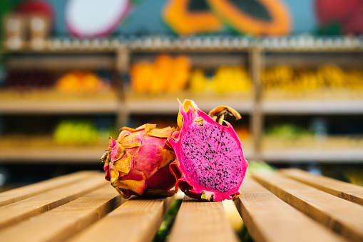 Close-up front view of fresh juicy pitahaya standing on wooden pallet at fruit and vegetables section of grocery store. Fresh exotic fruit selling in supermarket, selective focus, blurred background.