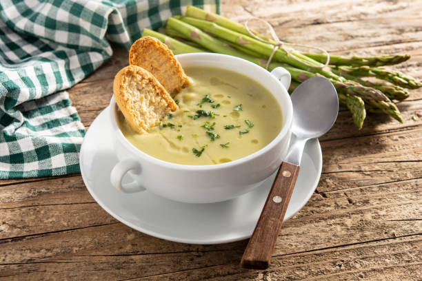 Fresh green asparagus soup in bowl on wooden table stock photo