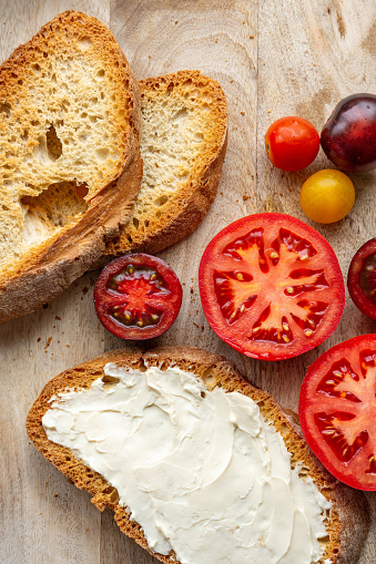 Top view of a toast spread with cream cheese and tomatoes cut in half on a wooden table
