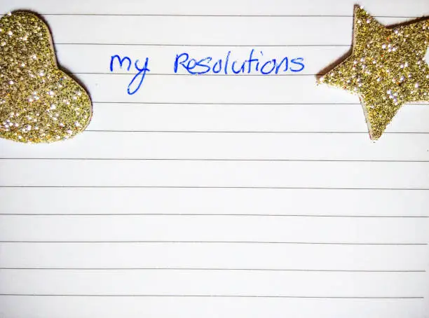 Photo of Silver glittery shapes (star, heart, ball) adorn a white paper for making resolutions.