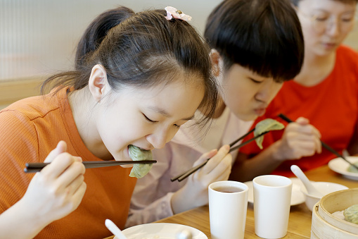 Two Asian teenage girls are enjoying vegetarian 'jiaozi' (Chinese dumpling) with their mother in restaurant.