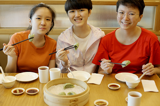 Two Asian teenage girls are enjoying vegetarian 'jiaozi' (Chinese dumpling) with their mother in restaurant.