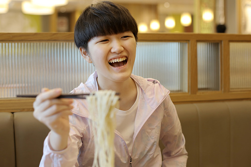 An Asian teenage girl is enjoying Chinese cuisine in restaurant.