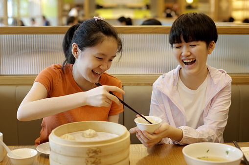 Two Asian teenage girls are enjoying 'xiao long bao' (Chinese soup dumpling) in restaurant.