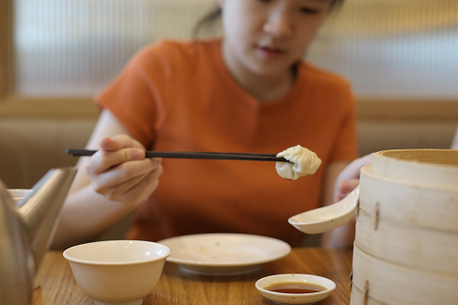 An Asian teenage girl is enjoying 'xiao long bao' (soup dumpling) in Chinese restaurant.