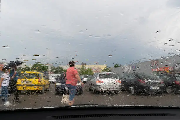 Raindrops on the window glass with outline of a car and a person