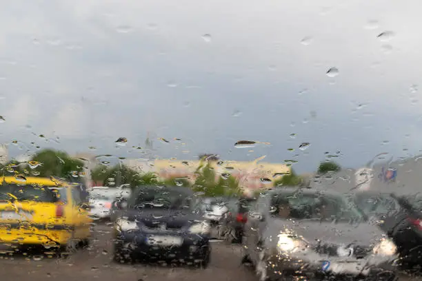 Raindrops on the window glass with outline of a car and a person