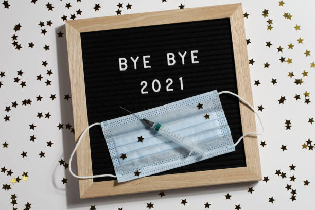 istock black letter board with text BYE BYE 2021 with small stars, syringe and mask on white background. Happy new ear 2022 concept. 1347062306
