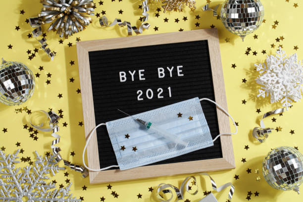 istock black letter board with text BYE BYE 2021 with decoration, syringe and mask on yellow background. Happy new ear 2022 concept. 1347062650