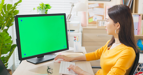 asian woman uses computer with green screen on desk