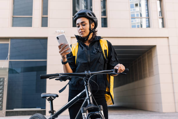 Courier with bike delivering food. Young courier checking delivery address on smartphone. stock photo