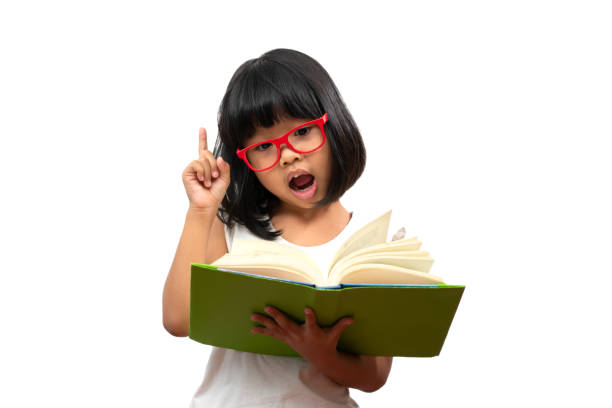 赤い眼鏡をかけた幸せなアジアの小さな幼稚園の女の子は、緑の本を持ち、白い孤立した背景に親指を立てて。小学校・幼稚園・ホームスクールにおける教育と教育の概念 - thumbs up book smiling student ストックフォトと画像