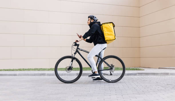 istock Side view of a young messenger with termal backpack man riding his bike and using mobile phone in the city 1347065873
