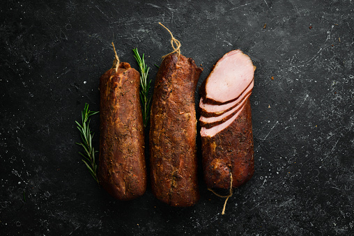 Smoked meats, smoked pork loin on a wooden table with addition of fresh herbs. On a black stone background. Top view. Free space for text.