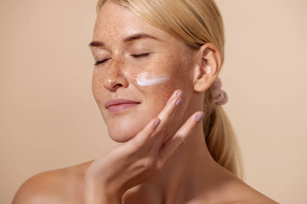 close up of beautiful young female with cream on a face. smiling woman with closed eyes touching cheek with fingers. - tratamento de pele imagens e fotografias de stock