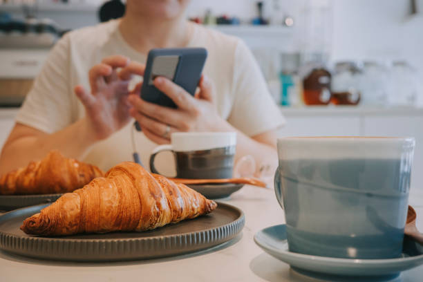 cropped shot mid-section of asian woman enjoying her croissant coffee at sidewalk cafe, taking photos of meal with smartphone sharing to social media before eating it. - gourmet enjoyment food freshness imagens e fotografias de stock